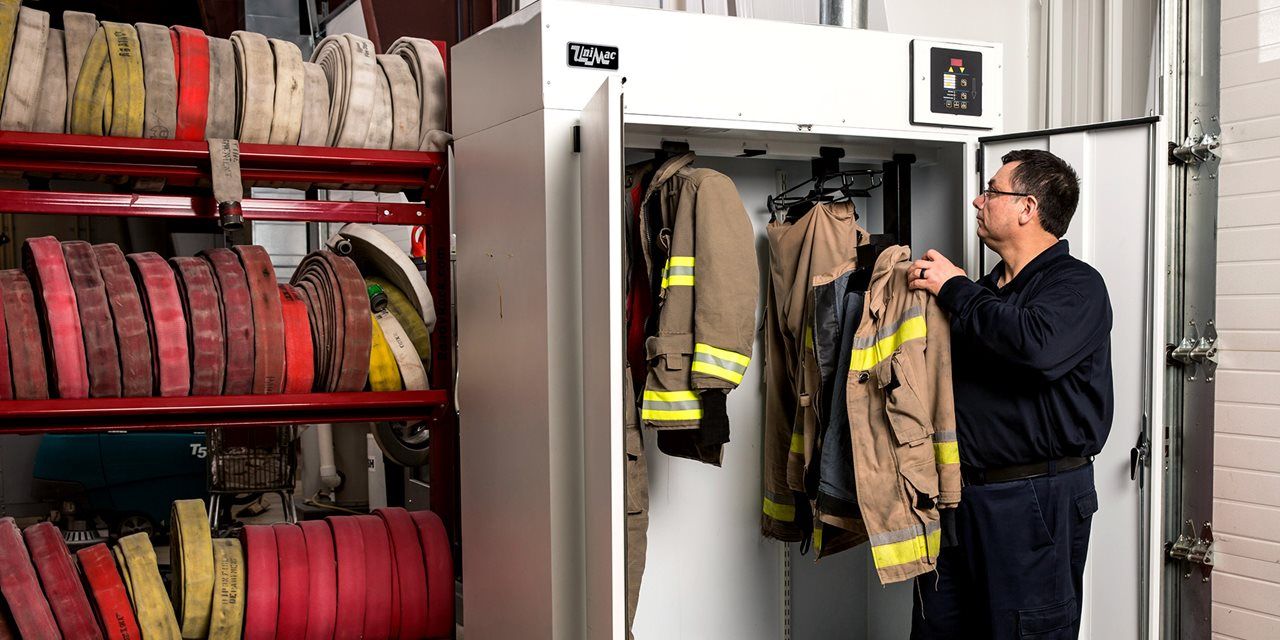 image of a firefighter hanging up a turnout coat in a UniMac PPE drying cabinett