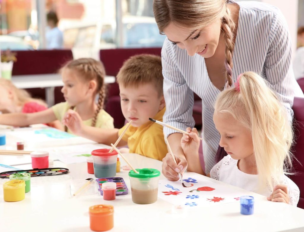 Women helping three children paint with watercolors