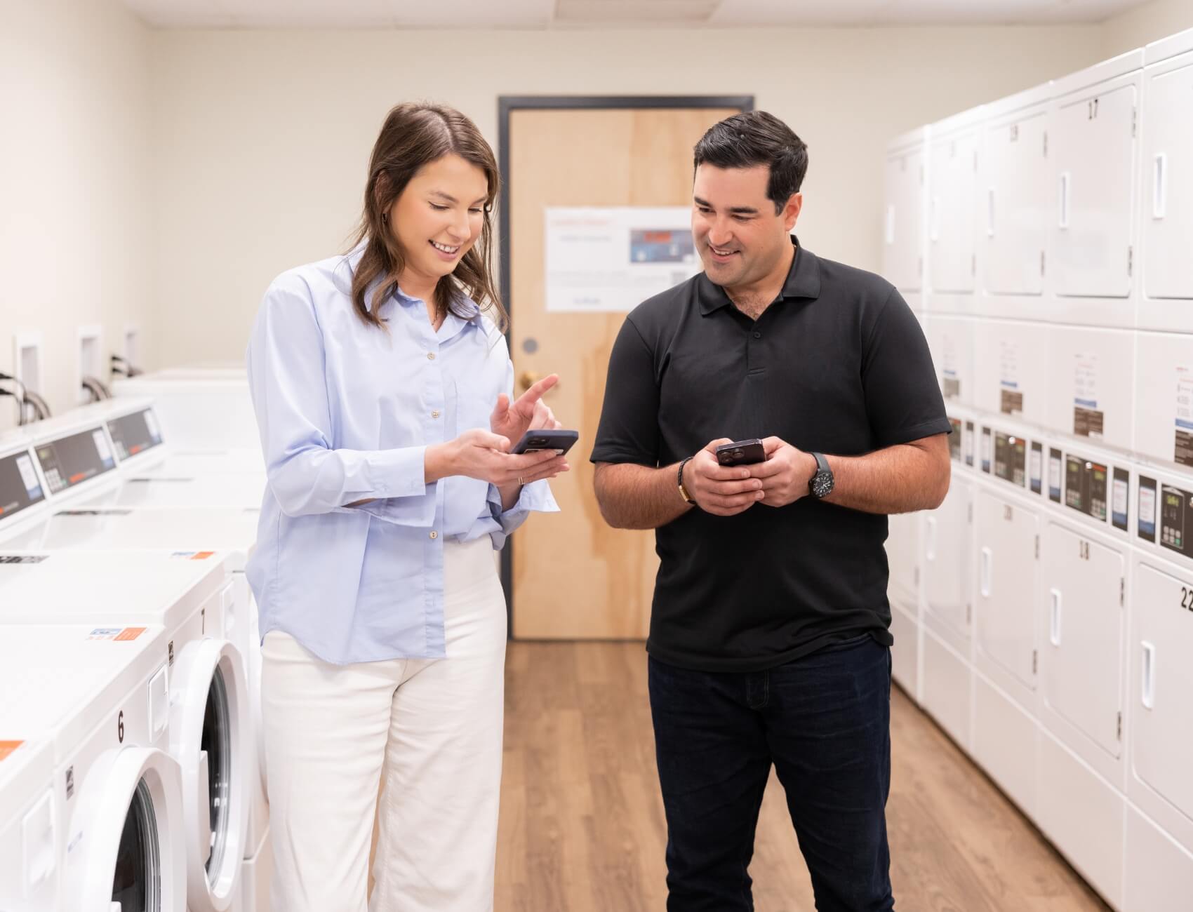 Two people using Speed Queen technology on phones in room of laundry equipment