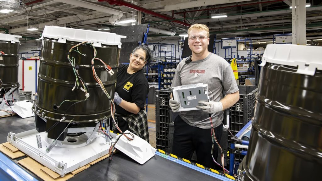 Two smiling employees working on washing machine drums in manufacturing facility