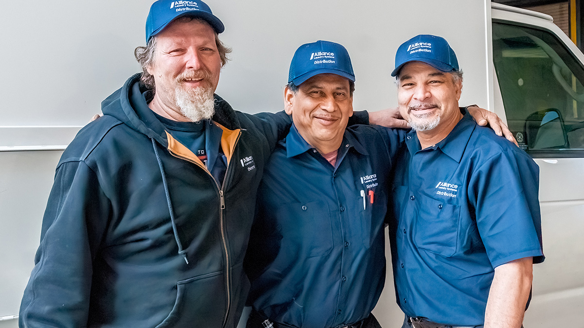 Three Alliance Laundry Distribution employees pose in front of van