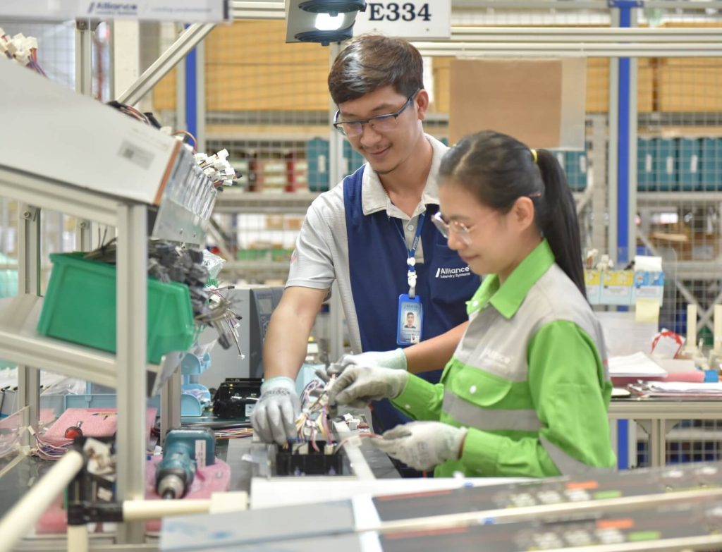Two Thai employees working together on machine part wiring
